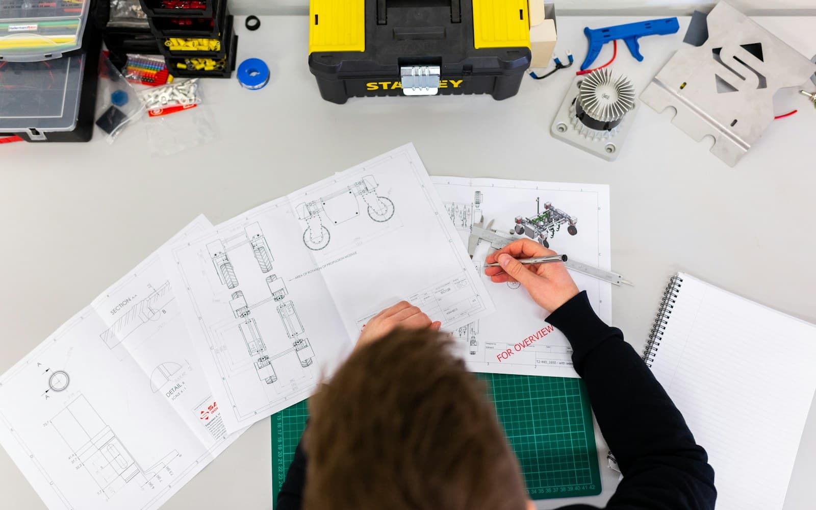 Hands measuring a technical drawing at a workshop desk.